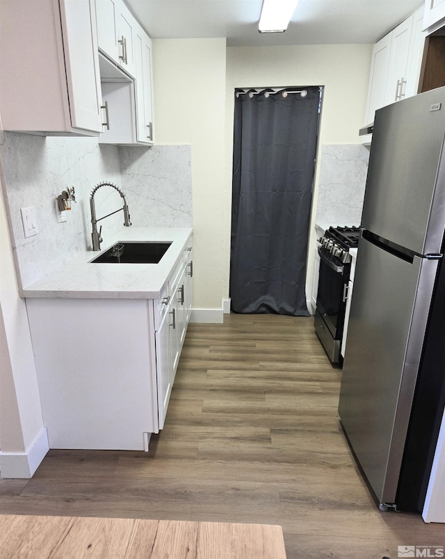 kitchen with freestanding refrigerator, a sink, range with gas stovetop, baseboards, and white cabinetry