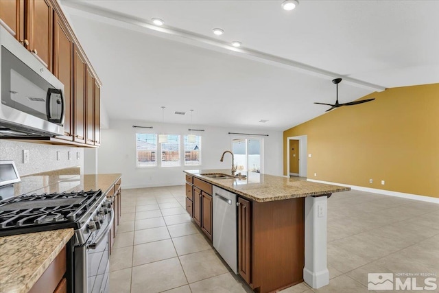 kitchen featuring light stone countertops, open floor plan, a sink, appliances with stainless steel finishes, and light tile patterned floors