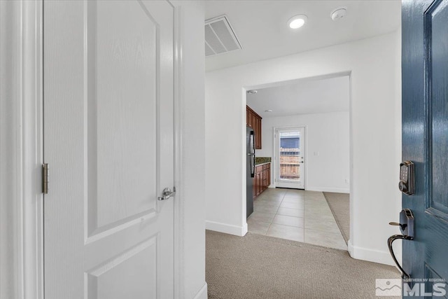 hall with visible vents, baseboards, light tile patterned floors, and light colored carpet