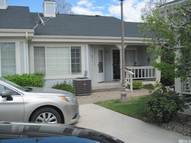 view of front facade with a porch, central AC unit, and a shingled roof