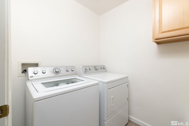 clothes washing area featuring washing machine and clothes dryer, baseboards, and cabinet space