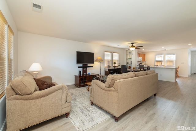 living room featuring light wood-type flooring, visible vents, a ceiling fan, and a healthy amount of sunlight