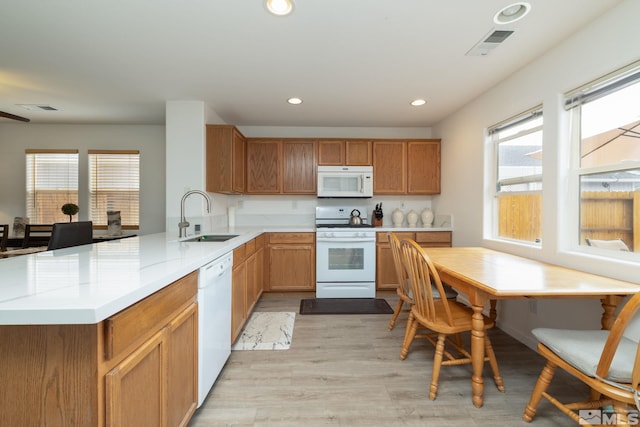 kitchen featuring a sink, a peninsula, white appliances, recessed lighting, and light wood finished floors
