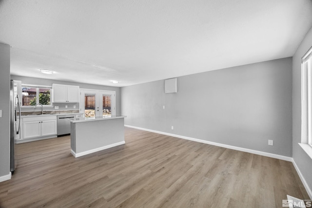 kitchen featuring light wood-type flooring, white cabinetry, light countertops, stainless steel dishwasher, and a kitchen island