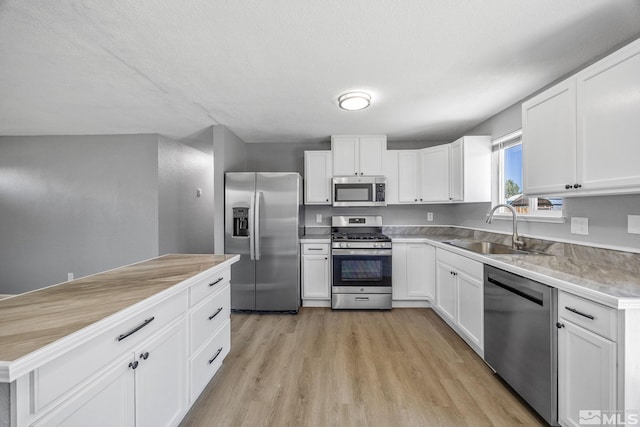kitchen with light wood-style flooring, a sink, stainless steel appliances, white cabinetry, and light countertops