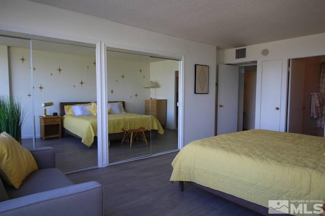 bedroom with a textured ceiling, visible vents, multiple closets, and dark wood-style floors