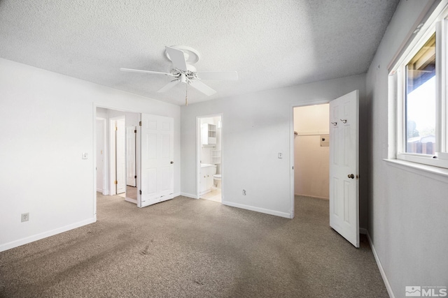 unfurnished bedroom featuring a spacious closet, baseboards, carpet, a textured ceiling, and connected bathroom