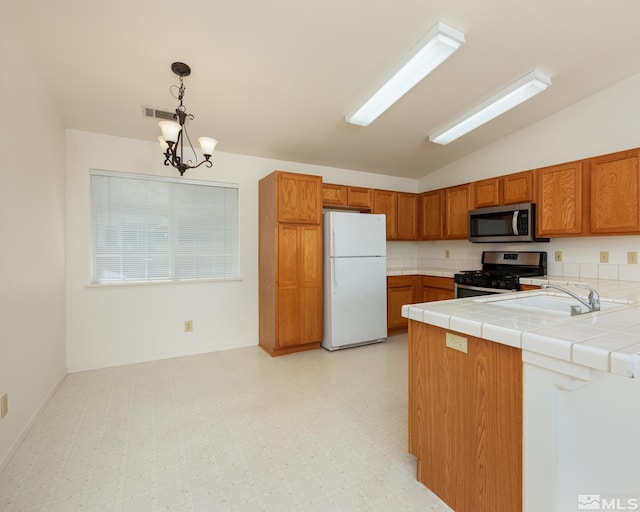 kitchen with stainless steel appliances, lofted ceiling, light flooring, brown cabinets, and a chandelier