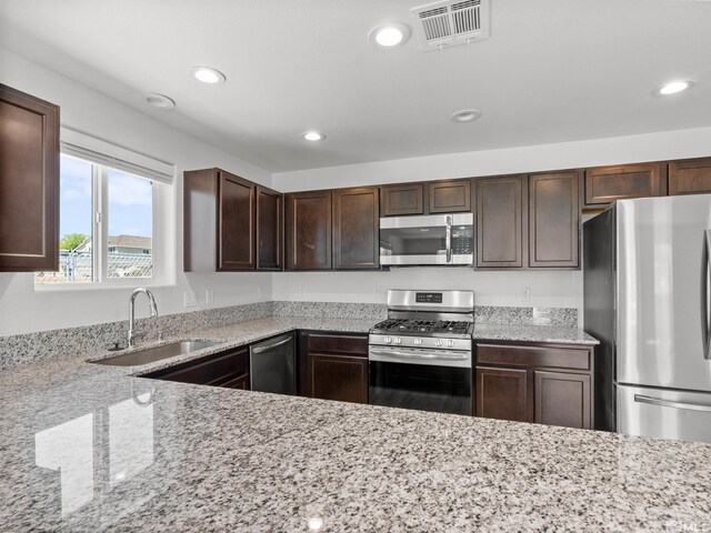 kitchen featuring stainless steel appliances, a sink, recessed lighting, dark brown cabinetry, and light stone counters