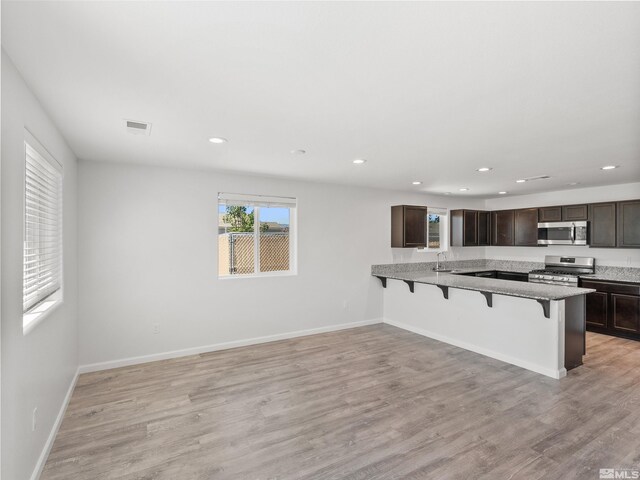 kitchen featuring stainless steel appliances, a breakfast bar area, a sink, recessed lighting, and dark brown cabinetry