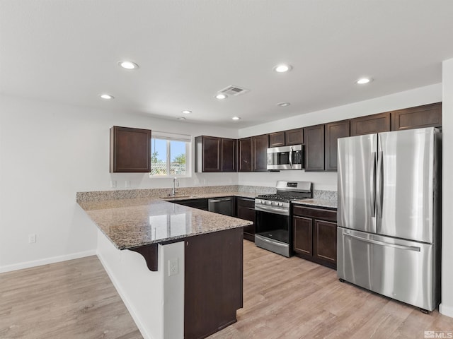 kitchen with appliances with stainless steel finishes, dark brown cabinetry, a peninsula, light stone countertops, and recessed lighting