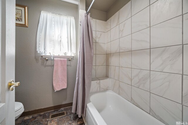 full bathroom featuring toilet, shower / tub combo, baseboards, and stone finish flooring