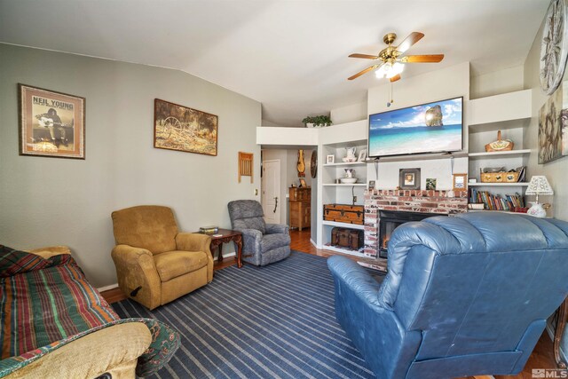 living area featuring a ceiling fan, lofted ceiling, a brick fireplace, wood finished floors, and baseboards
