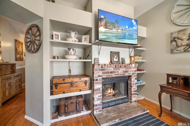 living room with wood finished floors, a brick fireplace, and baseboards