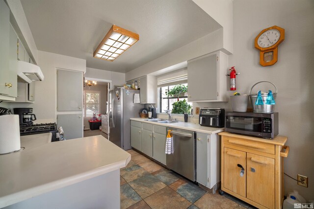 kitchen with appliances with stainless steel finishes, under cabinet range hood, a sink, light countertops, and stone finish flooring