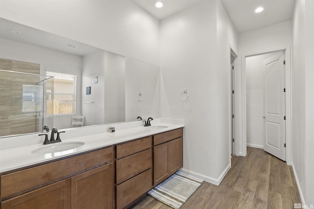 bathroom with a stall shower, wood finished floors, double vanity, and baseboards