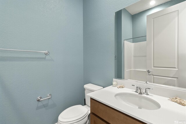 bathroom with toilet, vanity, and a textured wall