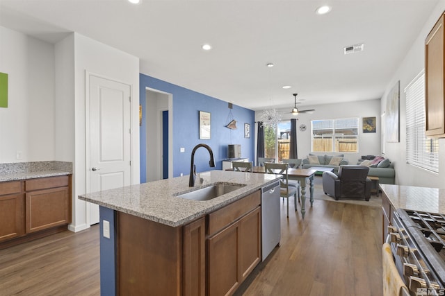kitchen with a sink, stainless steel appliances, wood finished floors, brown cabinets, and open floor plan