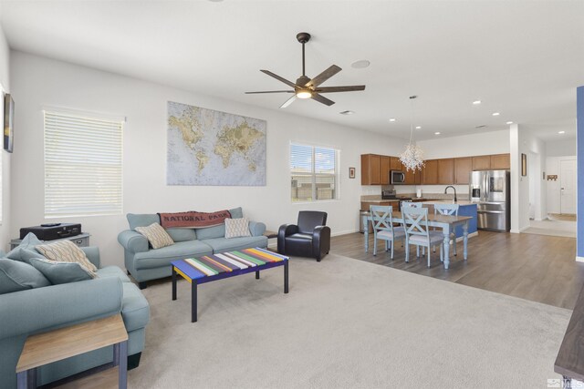 living area with a ceiling fan, recessed lighting, light carpet, a chandelier, and light wood-style flooring