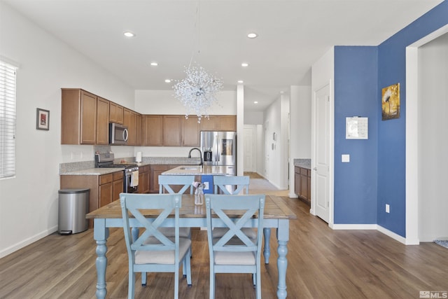kitchen featuring appliances with stainless steel finishes, wood finished floors, an island with sink, baseboards, and recessed lighting