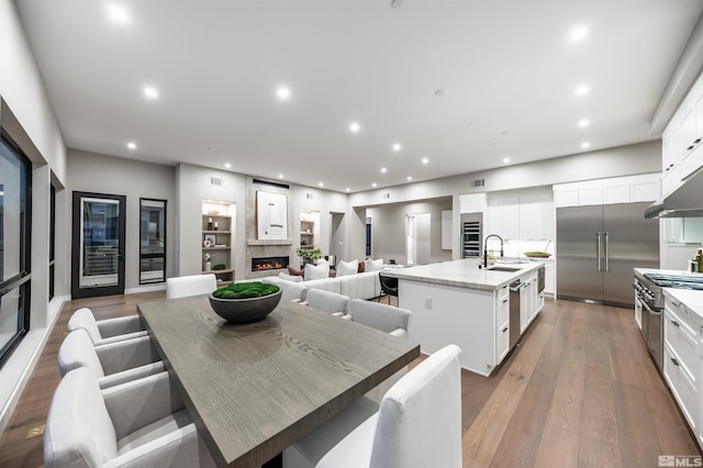 dining space featuring recessed lighting, a warm lit fireplace, light wood-type flooring, and wine cooler