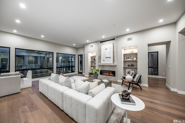 living area with a premium fireplace, baseboards, built in features, wood-type flooring, and recessed lighting