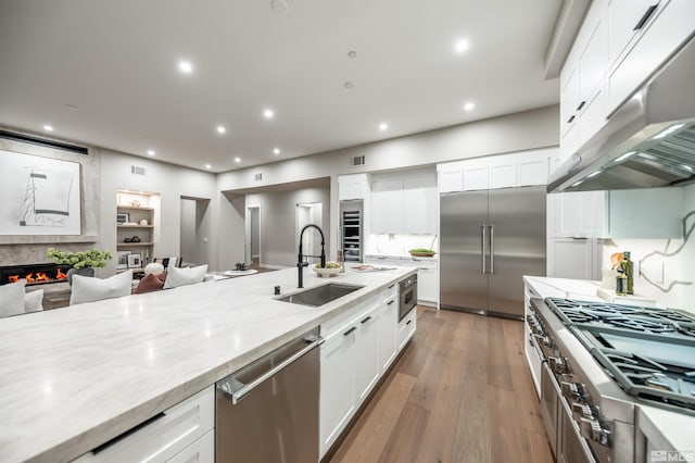kitchen featuring a sink, appliances with stainless steel finishes, under cabinet range hood, light stone countertops, and wine cooler