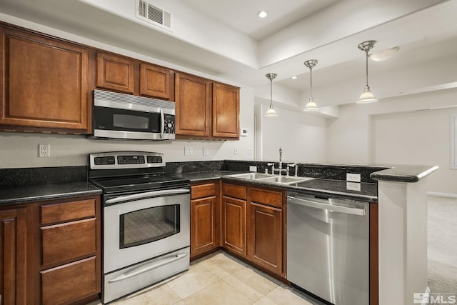 kitchen featuring stainless steel appliances, a sink, a peninsula, decorative light fixtures, and brown cabinetry