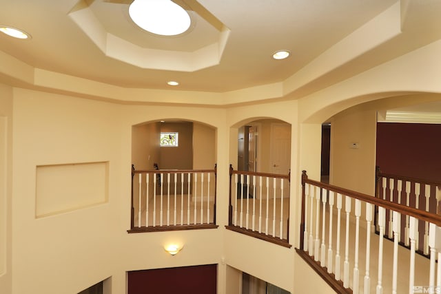 hallway featuring a raised ceiling, recessed lighting, and an upstairs landing