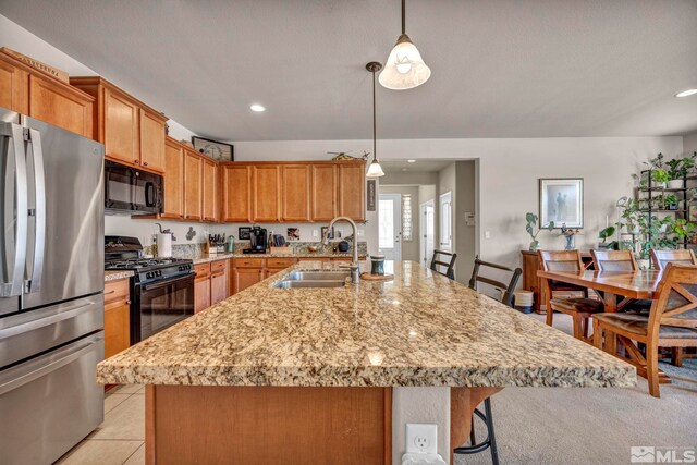 kitchen featuring black appliances, a sink, a kitchen bar, a kitchen island with sink, and light stone counters