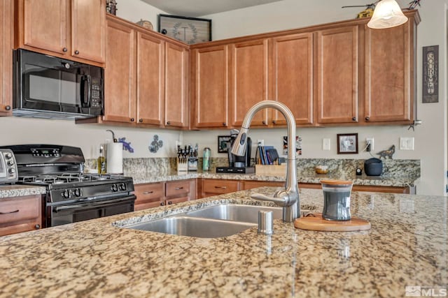 kitchen featuring black appliances, light stone countertops, a sink, and brown cabinets