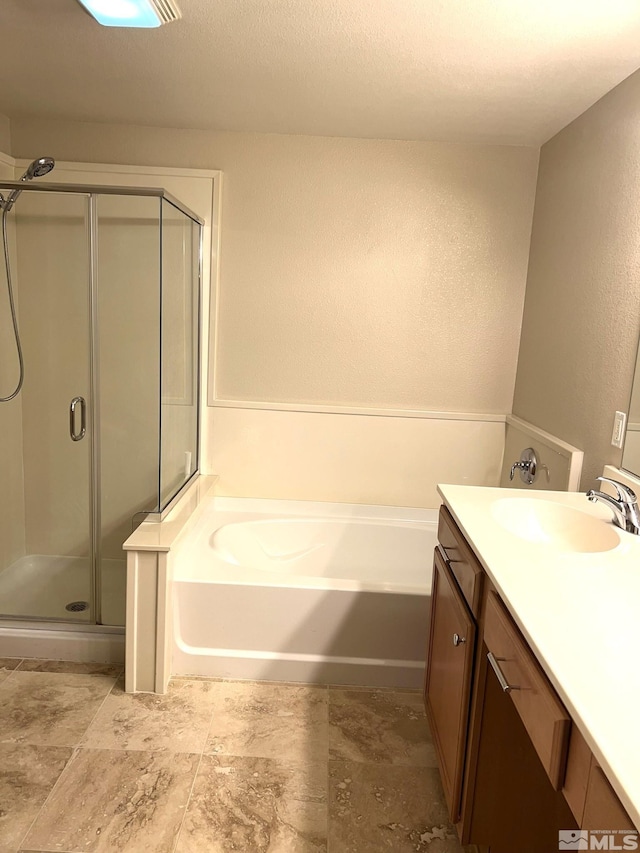 bathroom with a shower stall, a bath, vanity, and a textured wall