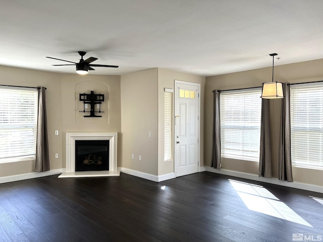 unfurnished living room with baseboards, a ceiling fan, dark wood-style floors, and plenty of natural light