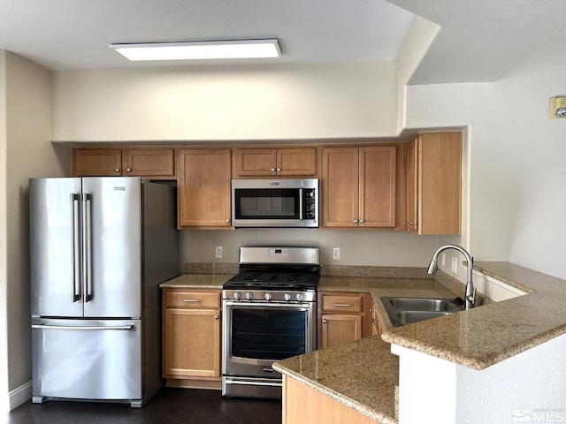 kitchen with appliances with stainless steel finishes, a sink, a peninsula, light stone countertops, and brown cabinets