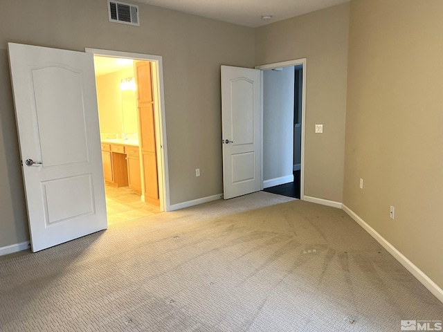 unfurnished bedroom with light carpet, baseboards, and ensuite bath