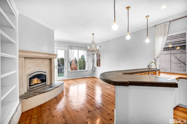 kitchen with ornamental molding, a chandelier, a lit fireplace, dark countertops, and light wood-style flooring