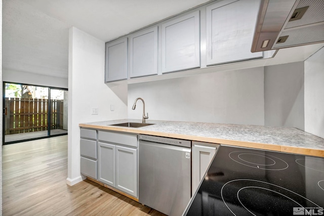 kitchen featuring stainless steel dishwasher, a sink, light wood-style floors, light countertops, and gray cabinets