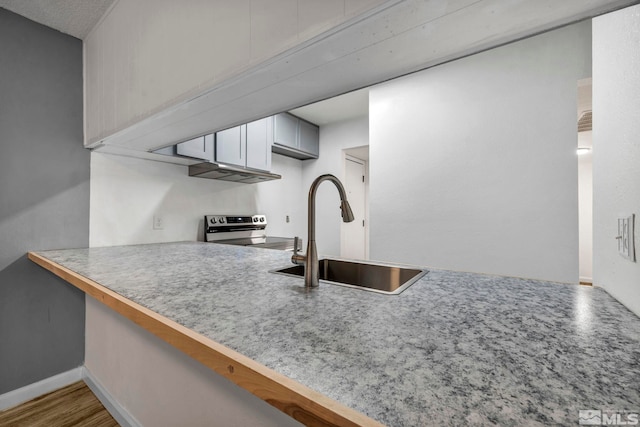 kitchen featuring a sink, stainless steel electric range oven, a peninsula, a kitchen bar, and baseboards