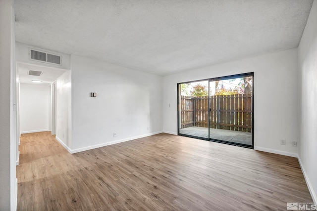 empty room featuring a textured ceiling, wood finished floors, and baseboards