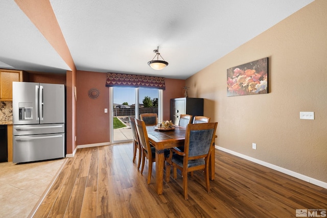 dining space featuring light wood-style floors, baseboards, and a textured wall