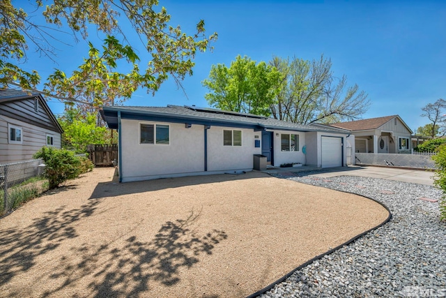 ranch-style house with fence, stucco siding, roof mounted solar panels, and an attached garage