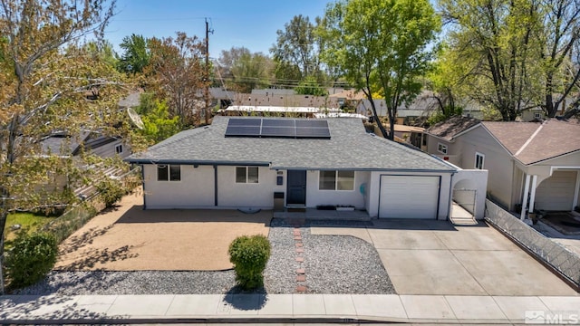 ranch-style home featuring a shingled roof, stucco siding, concrete driveway, roof mounted solar panels, and a garage