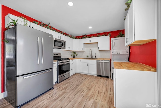 kitchen featuring appliances with stainless steel finishes, stacked washer / drying machine, a sink, wooden counters, and light wood-style flooring