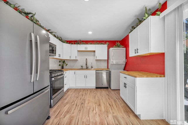 kitchen with appliances with stainless steel finishes, a sink, stacked washer / drying machine, light wood-style flooring, and decorative backsplash