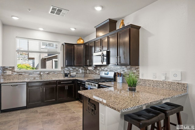 kitchen featuring appliances with stainless steel finishes, backsplash, light stone counters, a sink, and dark brown cabinets