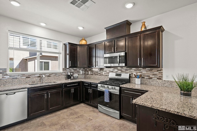 kitchen with stainless steel appliances, a sink, decorative backsplash, light stone countertops, and dark brown cabinets