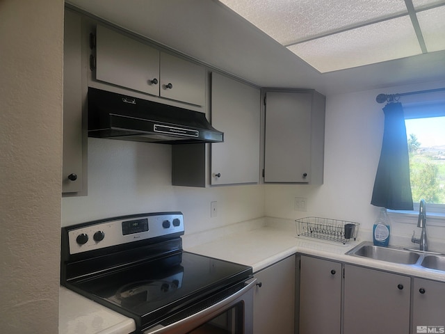 kitchen featuring stainless steel electric stove, under cabinet range hood, a sink, gray cabinetry, and light countertops
