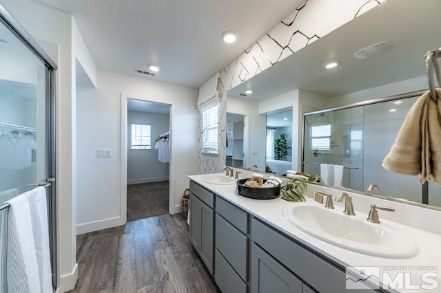 full bathroom with a stall shower, wood finished floors, double vanity, baseboards, and a walk in closet