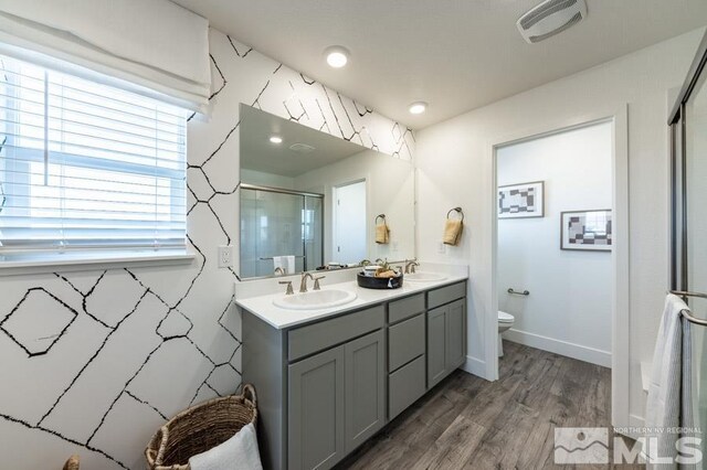 bathroom with a shower stall, toilet, wood finished floors, double vanity, and baseboards