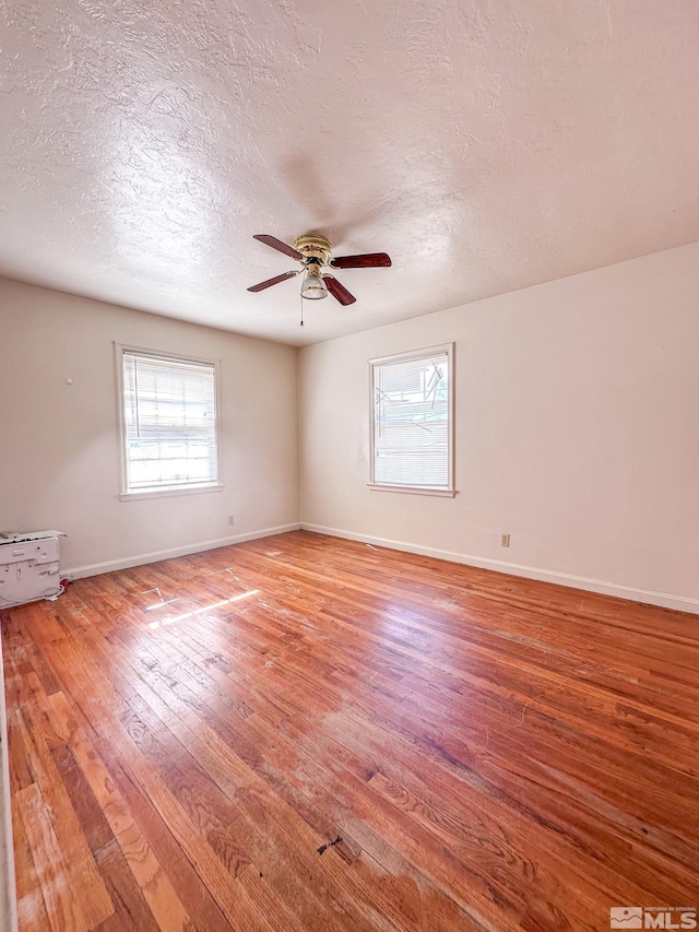 spare room with light wood-style flooring, a ceiling fan, a textured ceiling, and baseboards